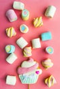 Scattered multi-colored marshmallows and gingerbread on a stick in the form of a muffin on a pink background.