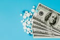 Scattered pharmaceutical medicine pills, tablets and capsules on dollar money isolated on blue background. Medicine expenses Royalty Free Stock Photo