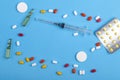 Scattered pills and medicines in blisters on a blue background and syringe copy place Royalty Free Stock Photo
