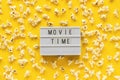 Scattered popcorn and lightbox text Movie time on yellow paper background. Top view Template