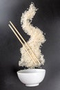 Scattered raw rice with wooden chopsticks and white bowl on black background Royalty Free Stock Photo