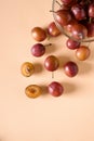 Scattered sliced half ripe sweet plum fruits with water drops near to plums in glass bowl on cream colored background Royalty Free Stock Photo