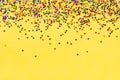 Scattered star shaped colorful glittering confetti over yellow background. Copy space.