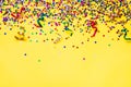 Scattered star shaped colorful glittering confetti and ribbons over yellow background. Copy space.