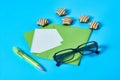 Scattered striped candies near green envelope with empty paper sheet, glasses, pen lies on blue desk. Love letter concept