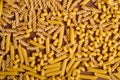 Scattered variety of uncooked golden wheat pasta on minimal brown background