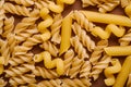 Scattered variety of uncooked golden wheat pasta on minimal brown background