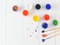 Scattered on a wooden table jars of gouache and three multi-colored brushes. Creative kit. Flat lay. Royalty Free Stock Photo