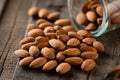Scattered almonds on rustic wooden surface with glass container Royalty Free Stock Photo