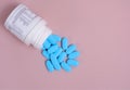 Scattering blue pills from bottle on pink background top view