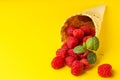 A scattering of fresh juicy natural raspberries with a sprig of mint in a waffle cone for ice cream. Minimalism on a yellow bright Royalty Free Stock Photo