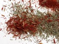 A scattering of particles of dried spicy spices and herbs of saturated fiery red, orange and green colors on a white background as