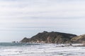 A scene of a beach on a cloudy day with mountain and road to the lighthouse, Nugget point, the Catlins, New Zealand I