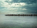 Scene with dramatic cloudy sky with sunrays, rocky pier with birds on a beautiful calm sea Royalty Free Stock Photo