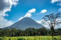 Scenery of a mountain in the middle of a green field touching the fluffy clouds