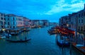 Scenery of romantic Venice in blue dusk, with tourists riding in a gondola on Grand Canal & ferry boats parking by restaurants