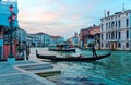 Scenery of romantic Venice at sunset, with view of a gondolier steering his ferry gondola by a pier, a vaporetto waterbus