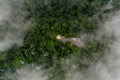 Scenic aerial view through the cloud looking at green forest and road