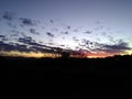 Scenic background. Orange, yellow, red and grey scattered clouds sunset above the silhouette of large trees and farm landscape