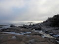 a rocky shore has ice melting from the water on it