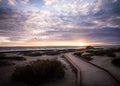 Scenic boardwalk alongside a sandy beach against a cloudy sky during a beautiful sunset