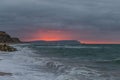 A scenic and dramatic sunset over a choppy sea with dark black thundery sky