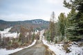 Scenic early spring view with snowy dirt road through the pass, green larch trees, snow and forest on the slopes against