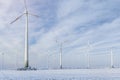 Scenic landscape view of white snowy frosty field and big modern wind turbine mill farm against beautiful blue clouds Royalty Free Stock Photo