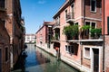 Scenic narrow canal with ancient buildings with potted plants in Venice, Italy