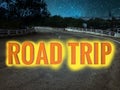 Scenic night landscape of country road at night with stars on the sky and the word ROAD TRIP written with orange and yellow color Royalty Free Stock Photo