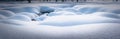 Scenic panorama of round fluffy snowdrifts on field with a wavy relief surface, small open, not frozen creek run between at forest Royalty Free Stock Photo