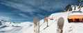 Scenic panoramic view of alpine peaks with ski lift ropeway on hilghland mountain winter resort and snow making machines on bright Royalty Free Stock Photo