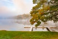 Scenic river edge and T-shaped pier under oak tree early morning fog just above the water level of Connecticut River with colorful Royalty Free Stock Photo