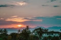 Scenic rose golden glowing Sunset. Half Sun hid in clouds above mountains. Close up view on palms, sea and mountains Royalty Free Stock Photo