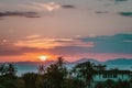 Scenic rose golden glowing Sunset. The whole Sun just above mountains. Close up view on palms, sea and mountains at horizon line. Royalty Free Stock Photo