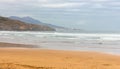 Scenic seascape with mountains and surfer. Cloudy sky above wide beach and mountain with big waves. Seaside in bay of Biscay.