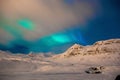 Scenic shot of the bright Northern Lights over a rocky mountain covered in snow