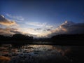 Scenic shot of fields and vegetation silhouettes under a cloudy sunrise with a heavenly effect