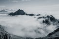 Scenic shot of rocky mountains in clouds under the clear sky, grayscale photography