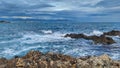 Scenic shot of sea waves slamming on a rocky beach under a cloudy gloomy sky