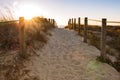 Scenic sunset on beach with wooden fence. Entrance to beach in evening sunlight. Wooden columns and path on sand. Royalty Free Stock Photo