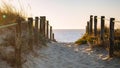 Scenic sunset on beach with wooden fence. Entrance to beach in evening sunlight. Wooden columns and path on sand.