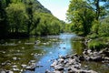 Scenic sun lit view along a calm river flowing between small rocks between trees