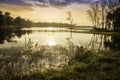 Scenic view at beautiful spring sunset with reflection on a shiny lake with  golden sun rays, calm water.  cloudy sky and glow on Royalty Free Stock Photo