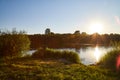 Scenic view at beautiful summer river or lake sunset with reflection on water with green grass, golden sun rays, calm Royalty Free Stock Photo