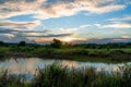 Scenic view of beautiful sunset above the lake at summer cloudy sky and grass field. Landscape of sunset and blue sky reflected on