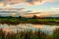 Scenic view of beautiful sunset above the lake at summer cloudy sky and grass field. Landscape of sunset and blue sky reflected on