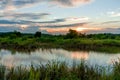 Scenic view of beautiful sunset above the lake at summer cloudy sky and grass field. Landscape of sunset and blue sky reflected on