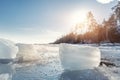 Scenic view of clear ice shard piece on coast of frozen lake landscape against warm sun shining rays through forest tree