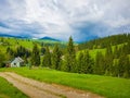 Scenic view of a cuontry road leading to an old village of wooden cabins on the hills of Carpathians. Sunny spring day with green Royalty Free Stock Photo